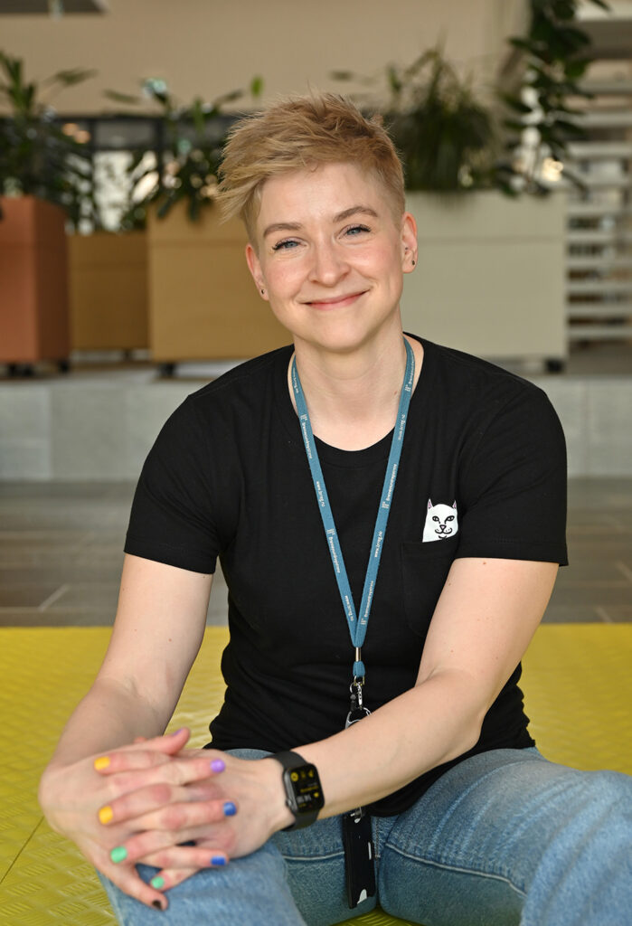 En ung kvinne med blondt hår smiler. Hun har på seg t-skjorte med katt på og hun holder hender foran seg. Neglene er lakket i fine farger.